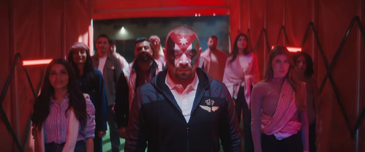 Wide scene delivered sideways in portrait raster: crowd in red-lit venue with foreground male performer wearing Jordan-flag face paint. No visible campaign title.