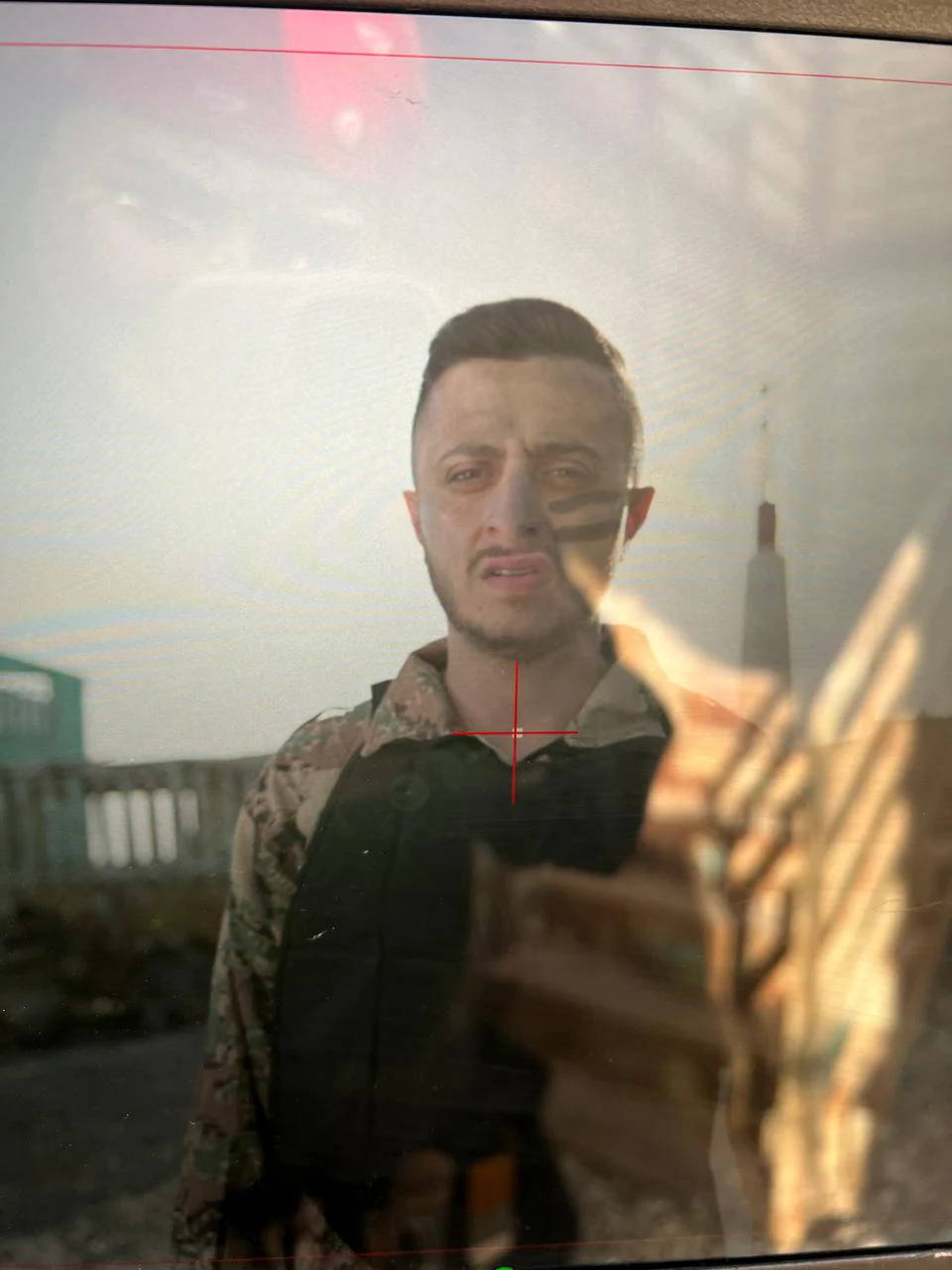 Production-monitor photograph of a performer with camouflage-pattern clothing and a dark cheek stripe; glare/reflections and camera framing marks are visible.